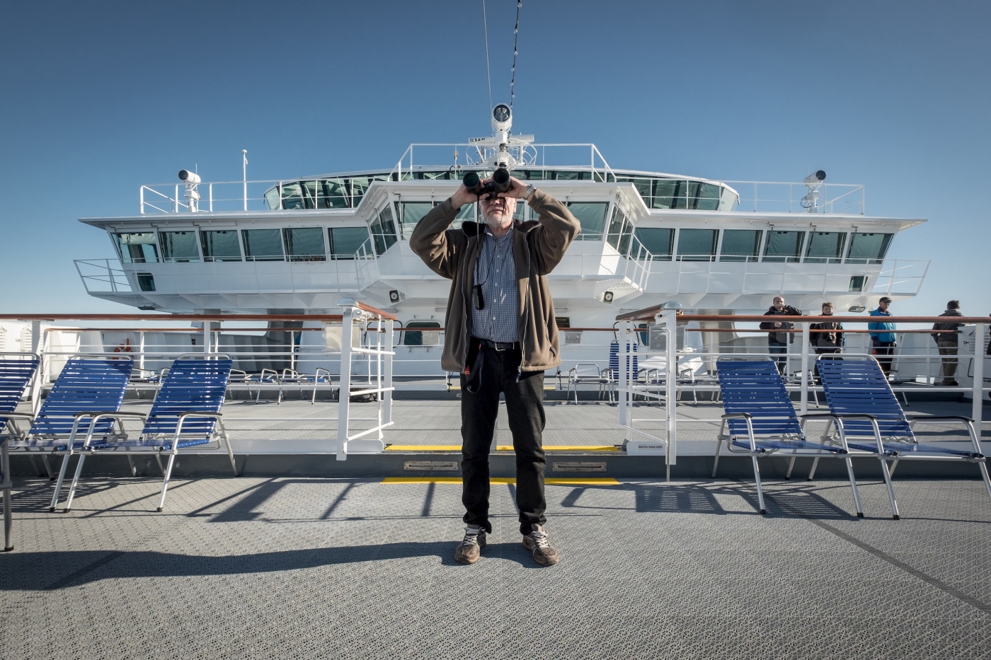 A cruise guest with binoculars on the deck of MS Fram in Greenland. By Mads Pihl