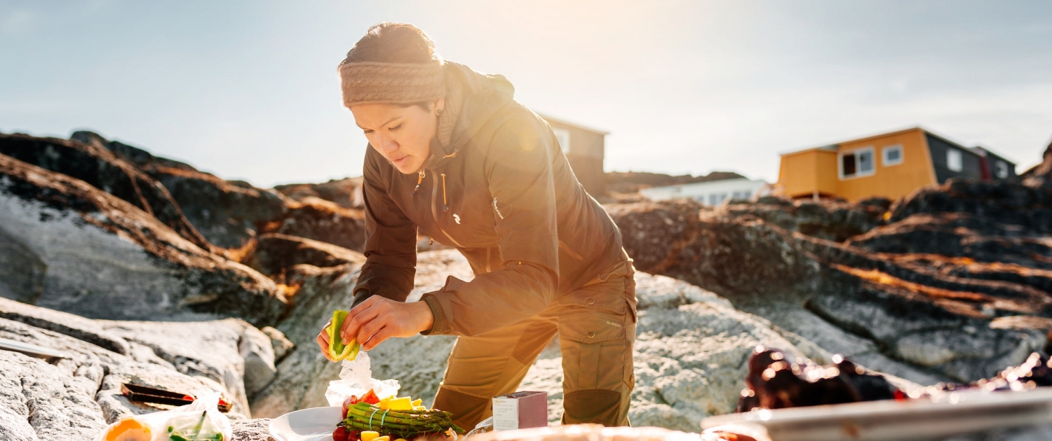 Woman preparing greenladic specialties on the rocks on the beach by Inuk Hostels in Nuuk in Greenland. Photo by Rebecca Gustafsson - Visit Greenland
