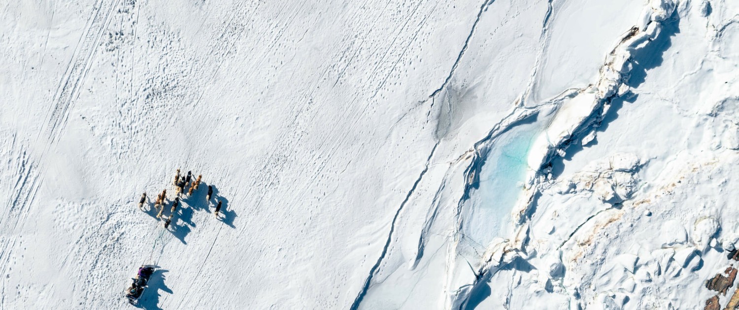Aerial view of sled dogs riding next to interesting features in the terrain - Photo by Alex Savu - Visit Greenland