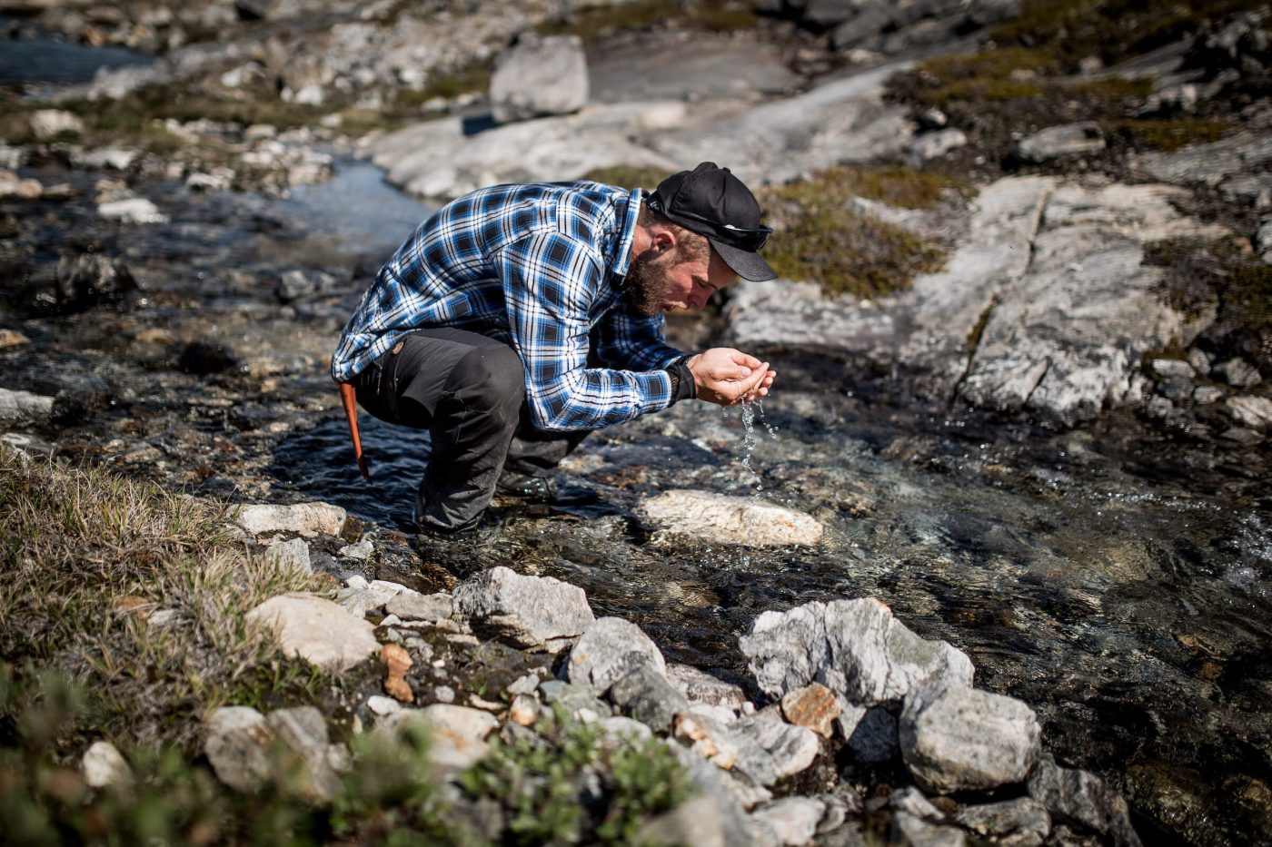 A hiker in East Greenland drinking pure, fresh water from a stream. Photo by Mads Pihl
