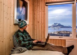 Traveler writes in his adventure log from the comfort of his bed at Inuk Hostels in Nuuk overlooking Nuuk Fjord and Sermitsiaq mountain. By Raven Eye Photography