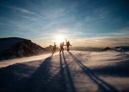 Skiers on the summit of a mountain with the sun setting. Photo by Joris Berthelot