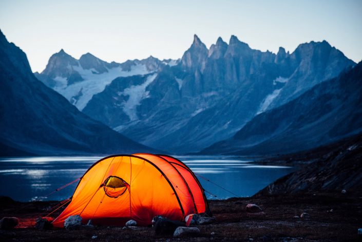 A lit tent at sunset looking north towards three peaks, Camp In Tasiilaq Fjord. By Chris Brinlee Jr