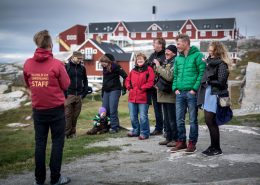 A tour guide entertaining guests on a town walk in Ilulissat in Greenland. By Mads Pihl
