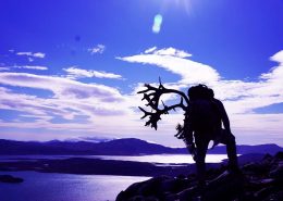 Purple landscape with a silhouette of a man carrying reindeer antlers on his back. Photo by Bowhunting Greenland