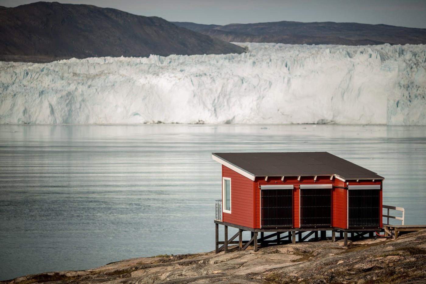 A comfort hut at Eqi Glacier Lodge with the glacier in the background in North Greenland. Photo by Mads Pihl - Visit Greenland