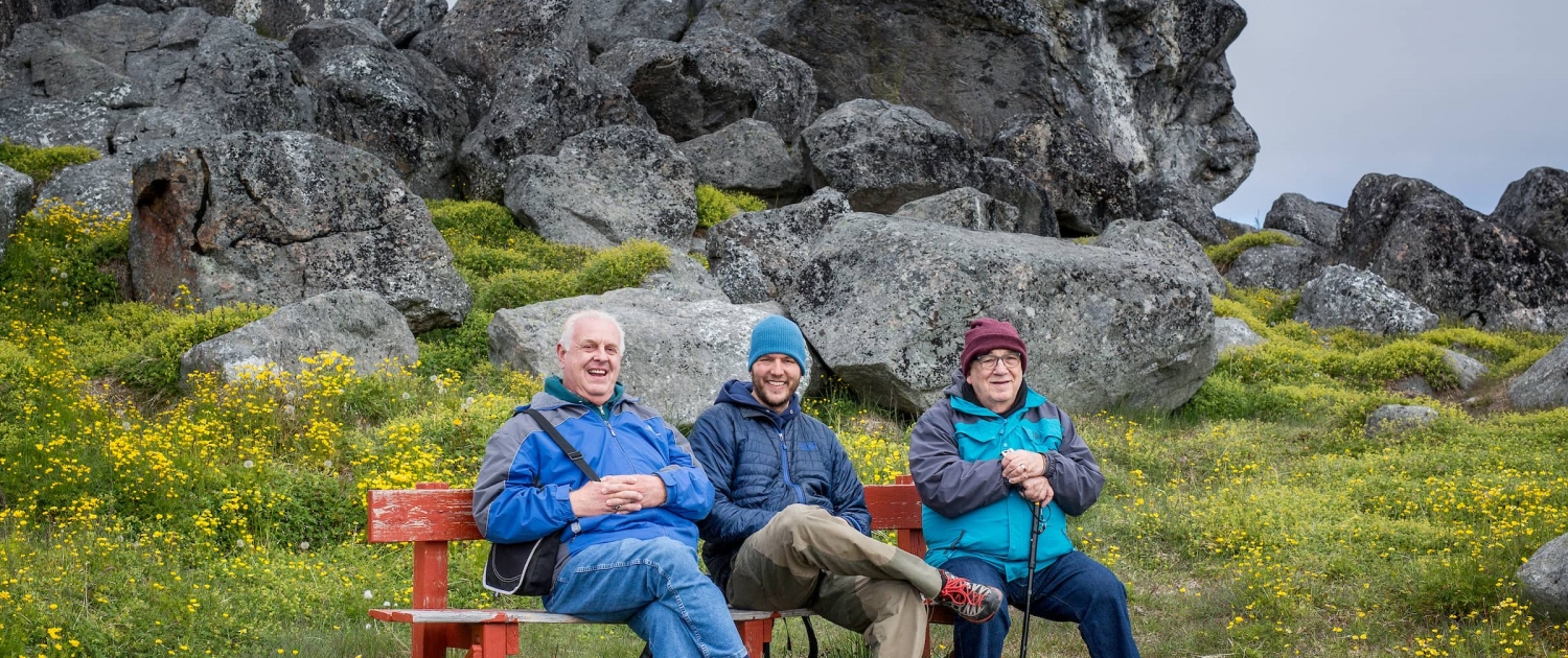 Cruise guests on a bench in front of the Knud Rasmussen rock in Nanortalik in South Greenland. Photo by Mads Pihl - Visit Greenland