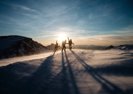 Skiers on the summit of a mountain with the sun setting. Photo by Joris Berthelot