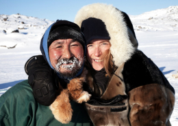 A dog sled driver and his happy passenger enjoying a day of dog sledding in Ilulissat in Greenland