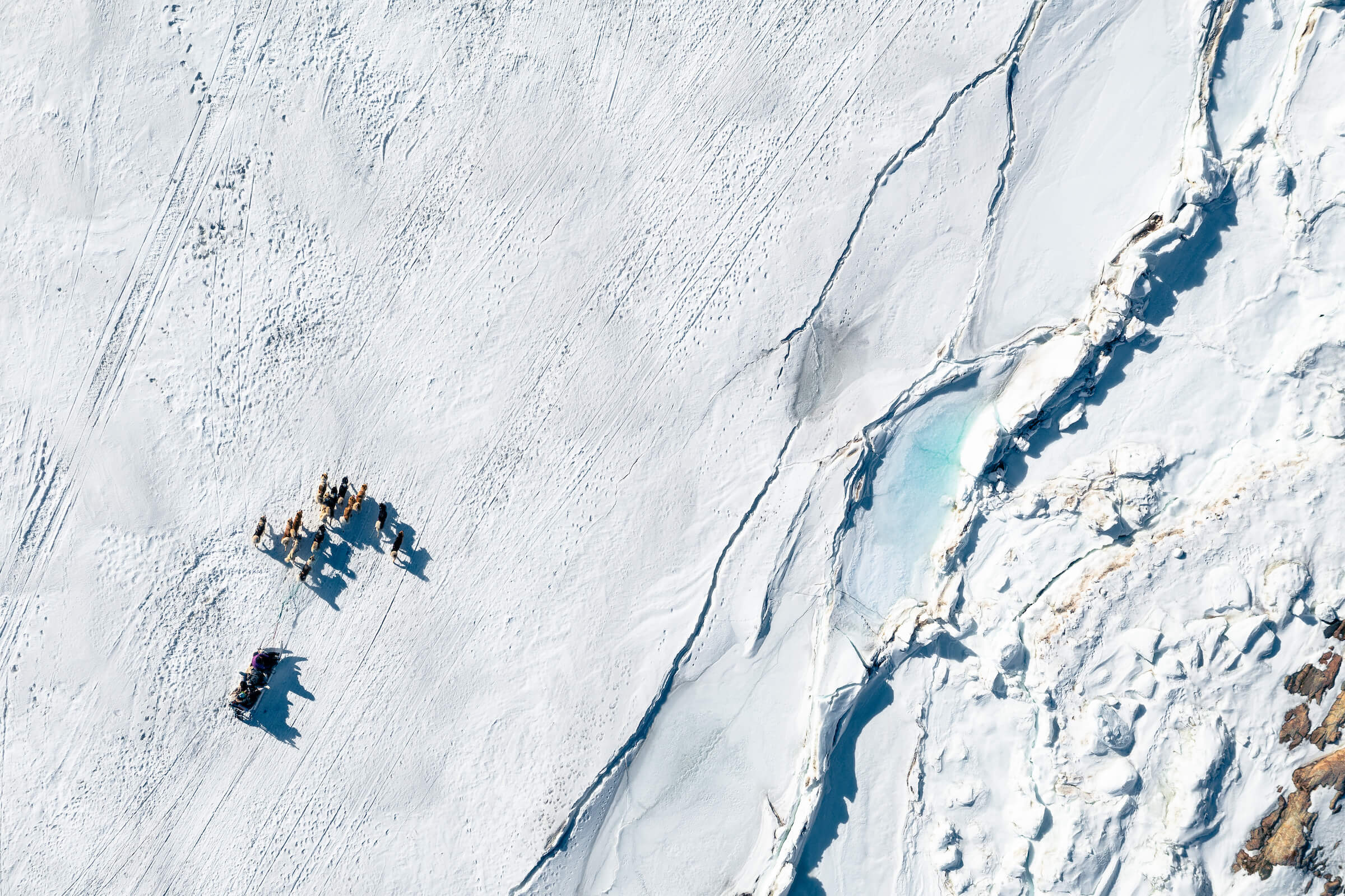 Aerial view of sled dogs riding next to interesting features in the terrain - Photo by Alex Savu - Visit Greenland