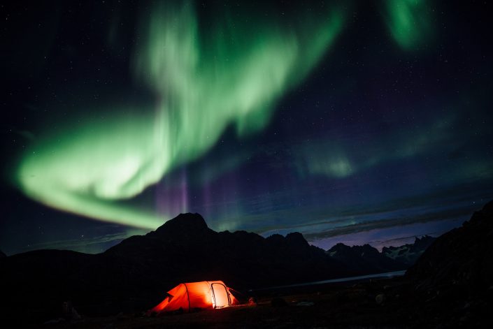 Northern lights over a lit tent, Camp In Tasiilaq Fjord. Photo by Chris Brinlee J