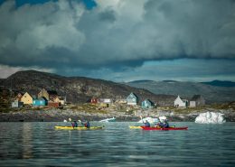 PGI Greenland kayakers paddling past Oqaatsut in the Disko Bay in Greenland. By Mads Pihl