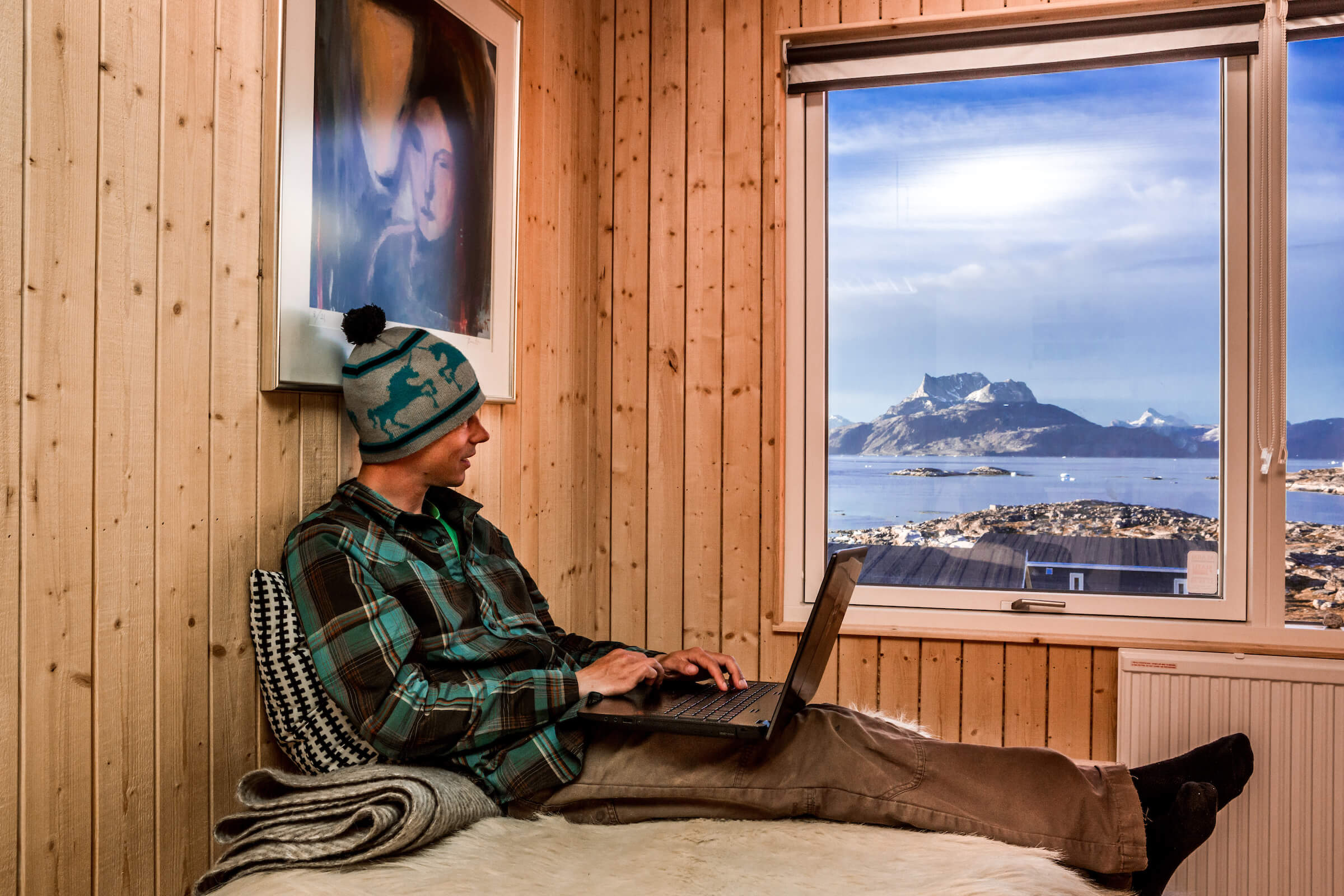 Traveler writes in his adventure log from the comfort of his bed at Inuk Hostels in Nuuk overlooking Nuuk Fjord and Sermitsiaq mountain. By Raven Eye Photography
